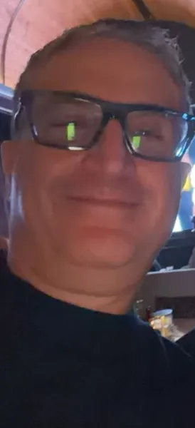 Andrew Hillman smiling in glasses and a black sweater during an evening out in Dallas